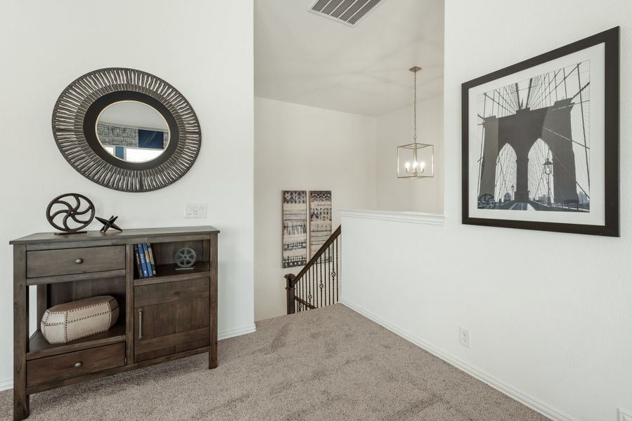 Upstairs hallway with dark wood console table, round mirror, pendant light, and staircase railing