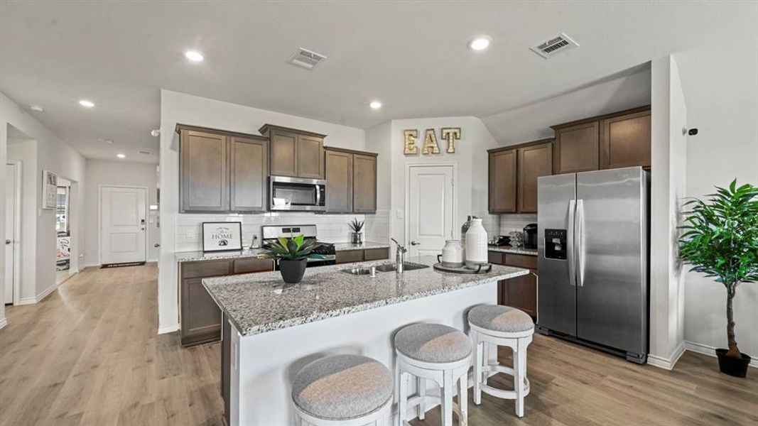 Kitchen featuring stainless steel appliances, light stone countertops, dark brown cabinets, backsplash, and light wood finished floors