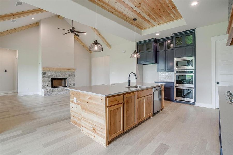 Kitchen with a stone fireplace, light wood-type flooring, a center island with sink, and stainless steel appliances