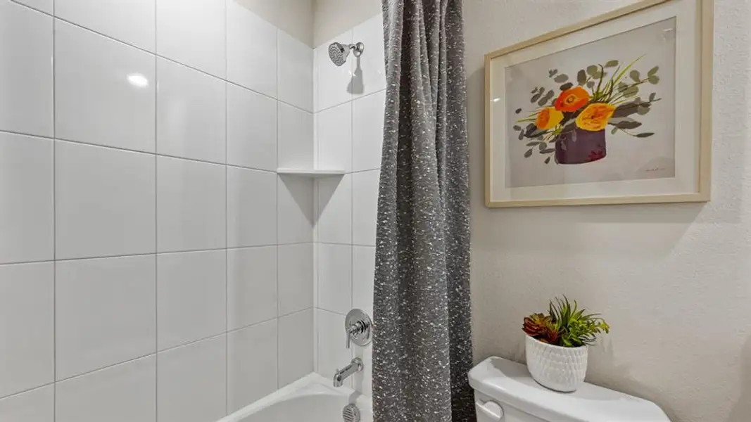 Full bathroom featuring shower / bath combination with curtain and a textured wall Full bathroom featuring shower / bath combination with curtain and a textured wall