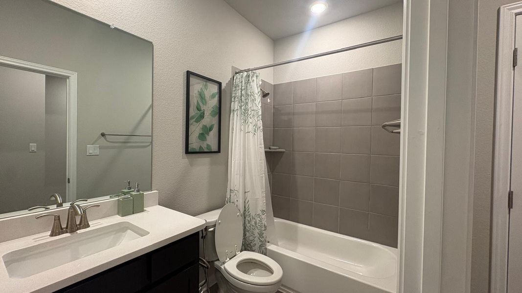A well-appointed bath features a sleek vanity, mirror, and a tiled shower-tub combination.