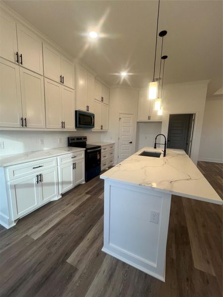 This modern kitchen features sleek white cabinetry, a large Quartz-patterned island with a built-in sink, stainless steel appliances, and elegant pendant lighting, all set on stylish medium gray/wood water proof plank flooring.
