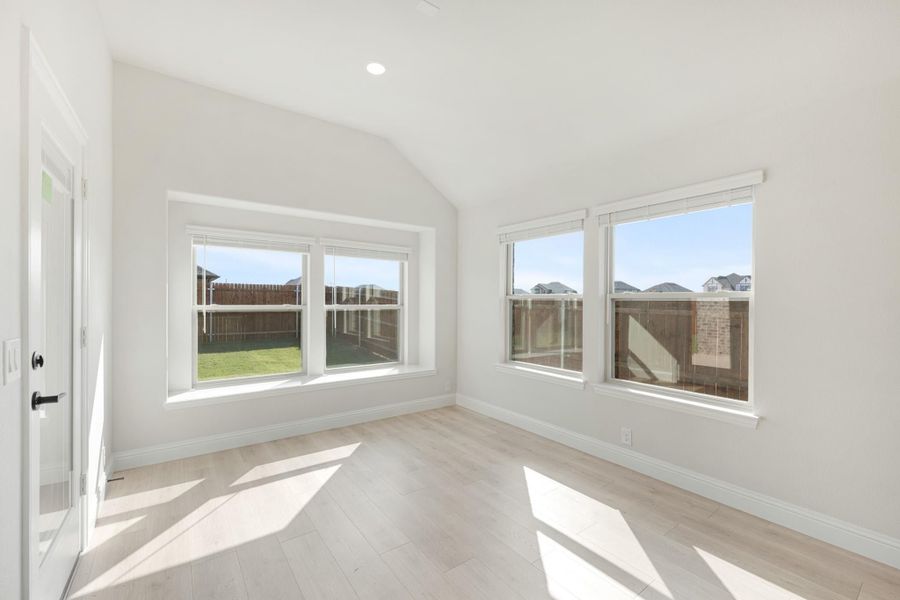 Empty room with vaulted ceiling, light wood floors, and large windows overlooking a fenced backyard