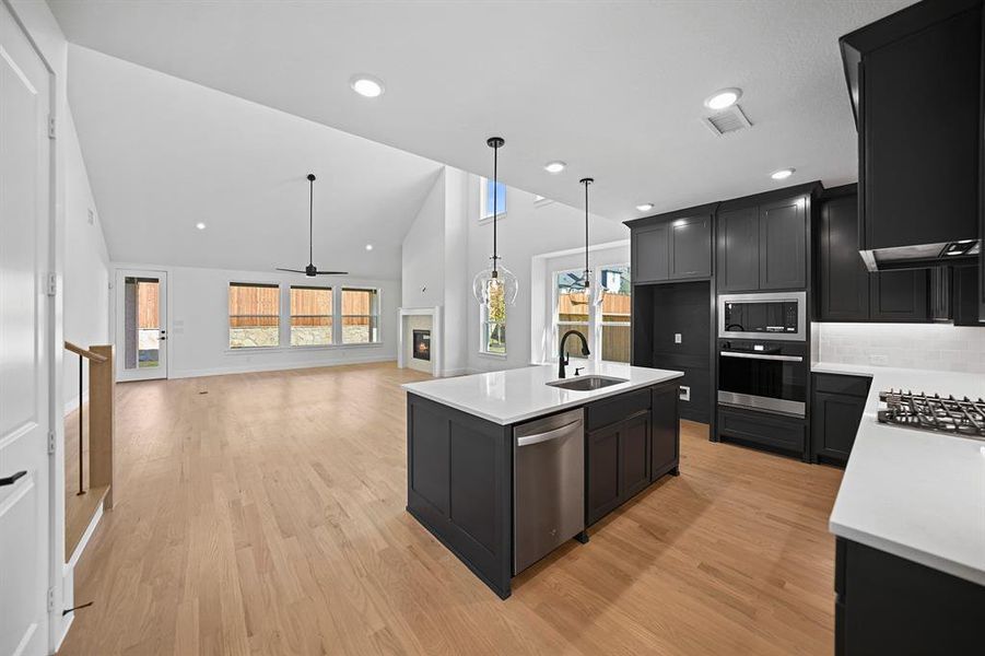Kitchen featuring dark cabinets, a kitchen island with sink, ceiling fan, high vaulted ceiling, and decorative backsplash Kitchen featuring dark cabinets, a kitchen island with sink, ceiling fan, high vaulted ceiling, and decorative backsplash