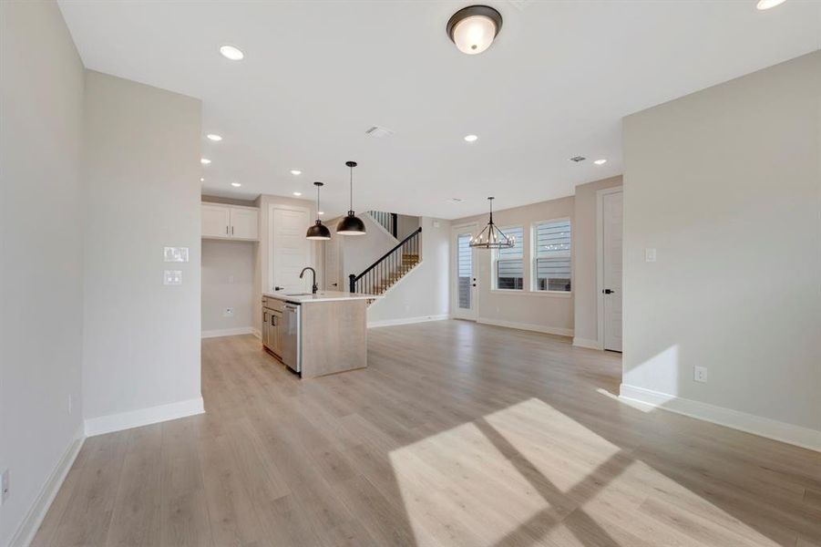 Unfurnished living room with light wood-type flooring and suspended lighting