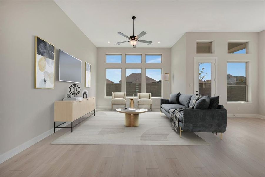 Spacious living area featuring light wood-finish flooring, high ceilings, abundant natural light from multiple windows, and a ceiling fan with integrated lighting