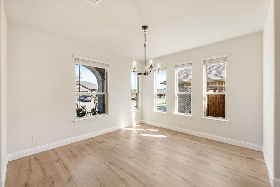 Empty dining room with light wood floors, chandelier, and multiple windows with natural light