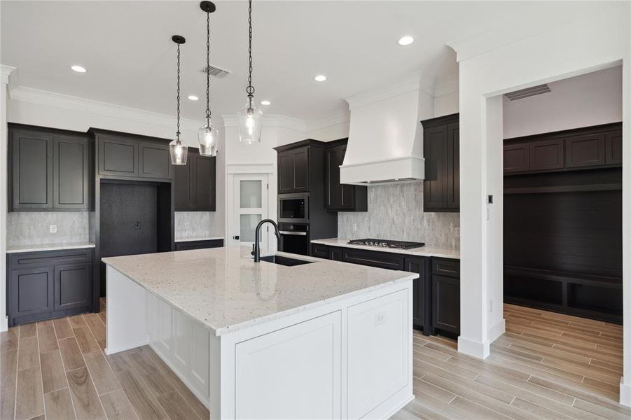 Kitchen featuring light hardwood / wood-style flooring, stainless steel appliances, an island with sink, light stone countertops, and decorative backsplash