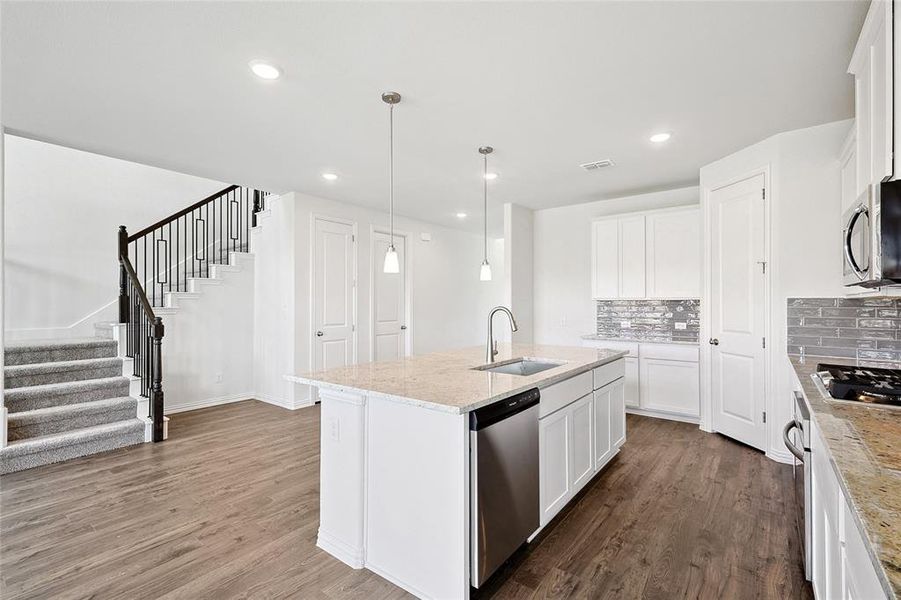 Kitchen with white cabinets, stainless steel appliances, wood-type flooring, and a kitchen island with sink