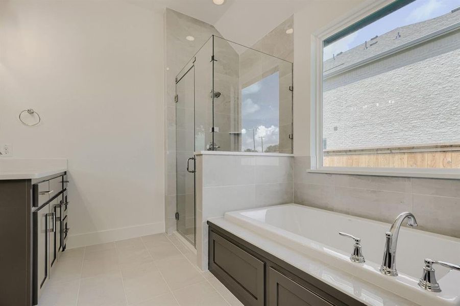 Bathroom featuring a built-in soaking tub with chrome fixtures, a glass-enclosed shower, a double vanity with dark cabinetry, and neutral tile flooring