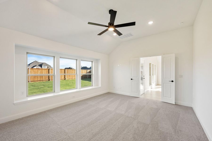 Empty bedroom with carpet, ceiling fan, triple windows, and vaulted ceiling overlooking backyard Empty bedroom with carpet, ceiling fan, triple windows, and vaulted ceiling overlooking backyard