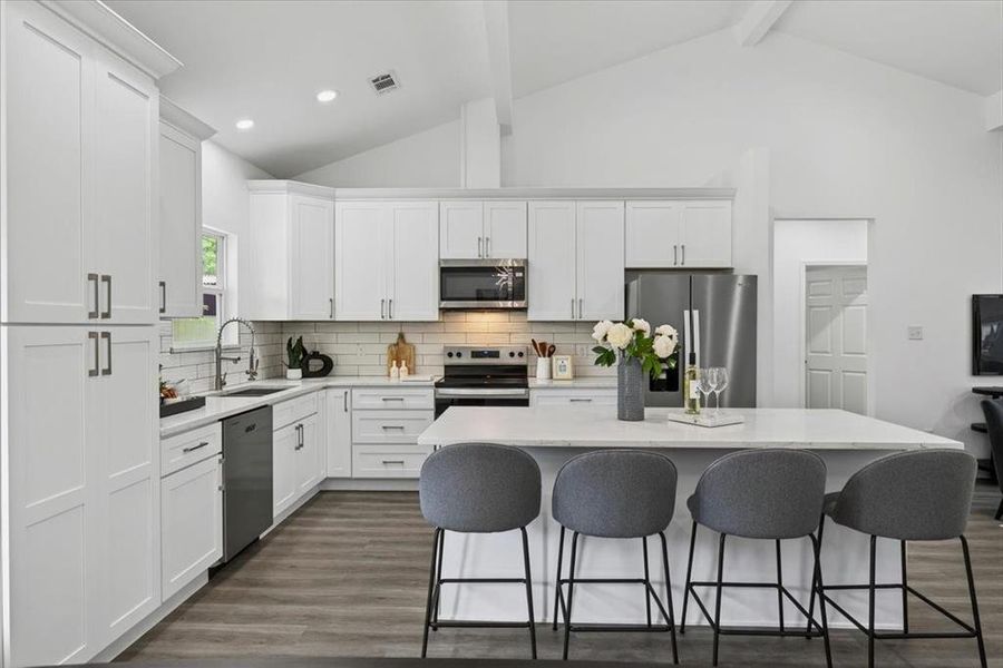 Well-appointed kitchen featuring a substantial island with countertop seating, stainless steel appliances, extensive white cabinetry, subway tile backsplash, and LVP flooring