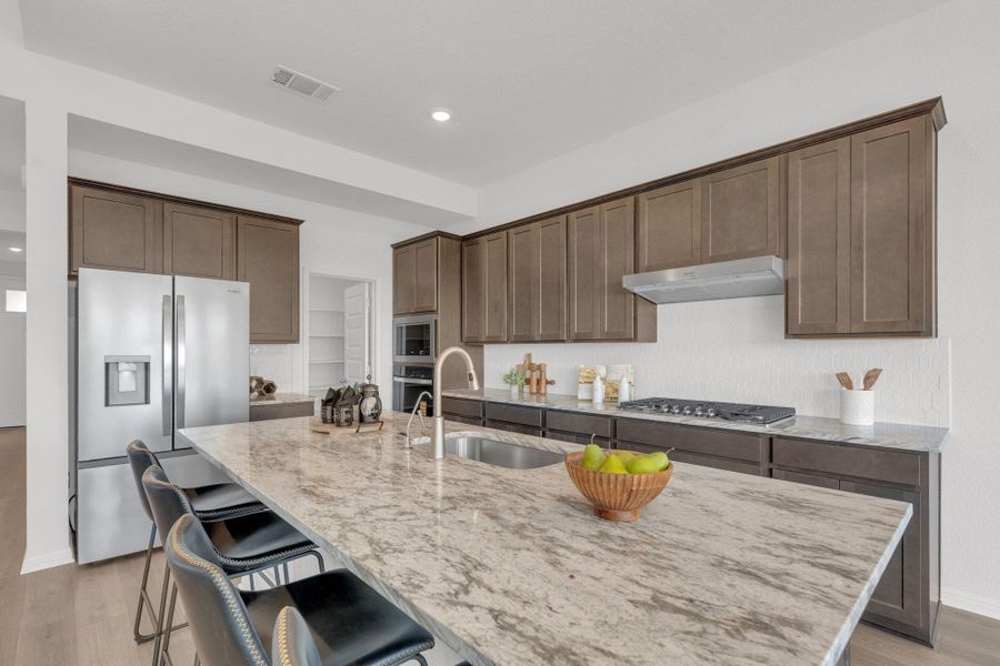 Kitchen featuring light wood-style floors, light stone counters, stainless steel appliances, a breakfast bar, and an island with sink Kitchen featuring light wood-style floors, light stone counters, stainless steel appliances, a breakfast bar, and an island with sink