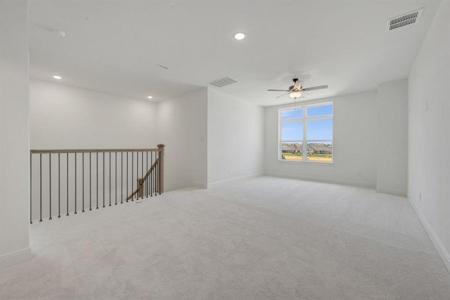 Spacious upper-level room featuring light gray carpeting, recessed lighting, a modern ceiling fan, and a large window
