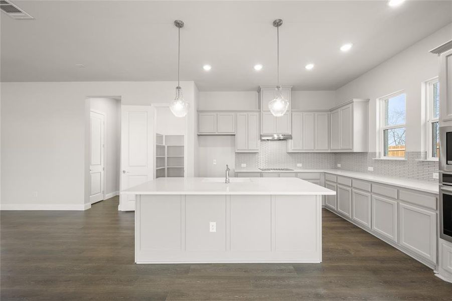 Kitchen featuring backsplash, recessed lighting, an island with sink, black electric stovetop, and light countertops Kitchen featuring backsplash, recessed lighting, an island with sink, black electric stovetop, and light countertops