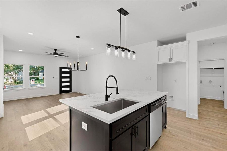 Kitchen with hanging light fixtures, light wood-style floors, open floor plan, white cabinets, and dishwasher Kitchen with hanging light fixtures, light wood-style floors, open floor plan, white cabinets, and dishwasher