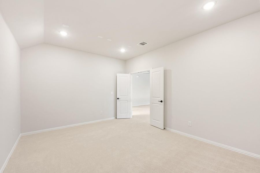 Empty bedroom with beige carpet, white walls, recessed lighting, and open double doors leading to a closet or hallway