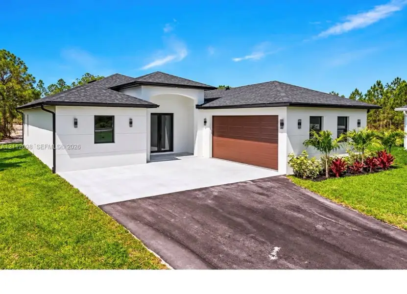 Single-story residence featuring a smooth stucco exterior, asphalt shingle roof, two-car garage with wood-finish door, concrete driveway, and professional landscaping Single-story residence featuring a smooth stucco exterior, asphalt shingle roof, two-car garage with wood-finish door, concrete driveway, and professional landscaping