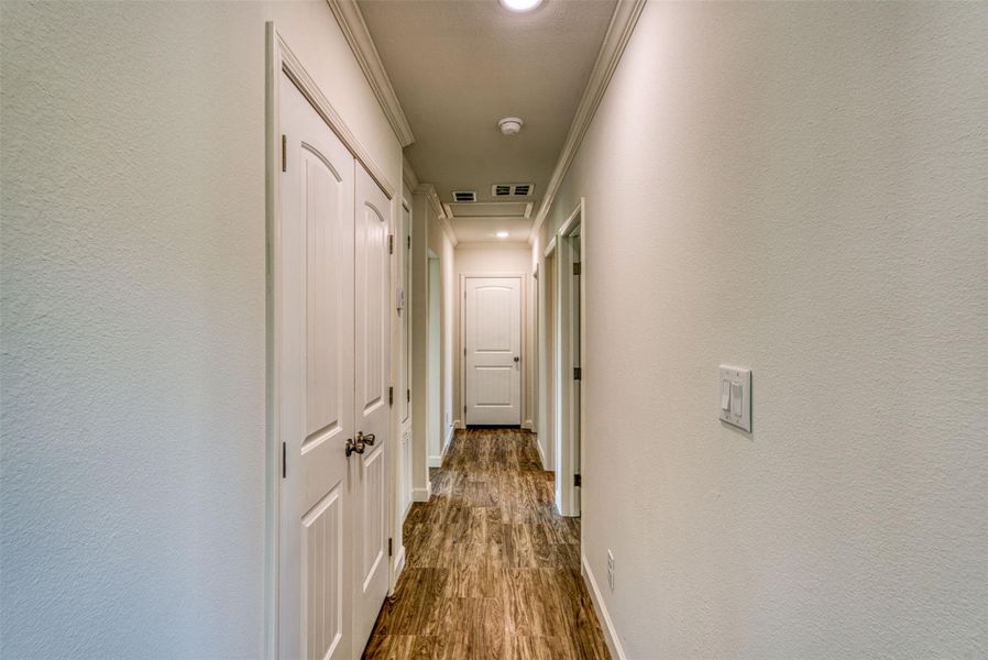 A well-lit corridor with crown molding and richly textured flooring provides seamless transitions between living spaces. A well-lit corridor with crown molding and richly textured flooring provides seamless transitions between living spaces.