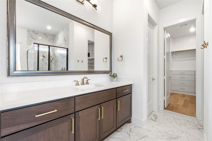 The Primary Bath vanity exudes modern elegance, combining dark custom cabinetry, striking gold-tone fixtures, and extensive surfaces for a polished, functional space.