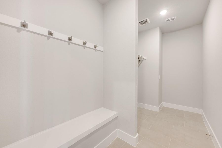 Mudroom with built-in bench, row of wall hooks, and tile flooring leading to a hallway Mudroom with built-in bench, row of wall hooks, and tile flooring leading to a hallway