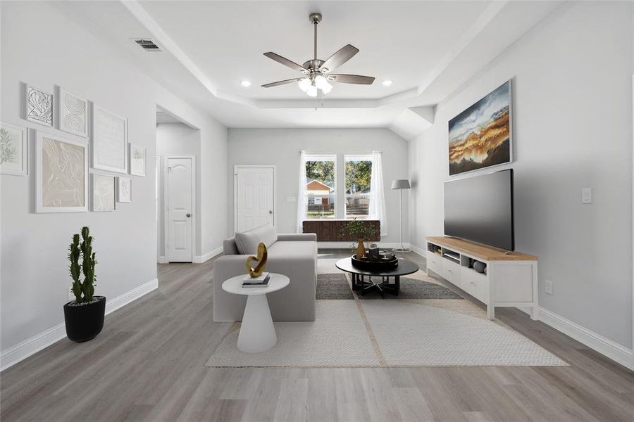 Living room featuring a raised ceiling, ceiling fan, and light wood-type flooring