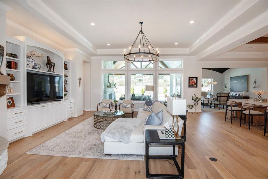 This elegant living space features an open floor plan with hardwood floors, a cozy seating area, and a stylish chandelier. Large windows allow plenty of natural light, while built-in shelving and a fireplace add charm. The room flows seamlessly into a dining area, perfect for entertaining.