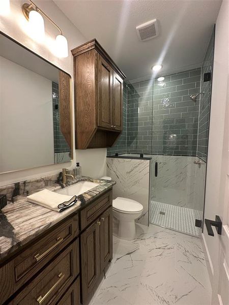 Bathroom featuring a dark wood-finish vanity with gold-tone hardware, a rectangular undermount sink, and a patterned stone countertop