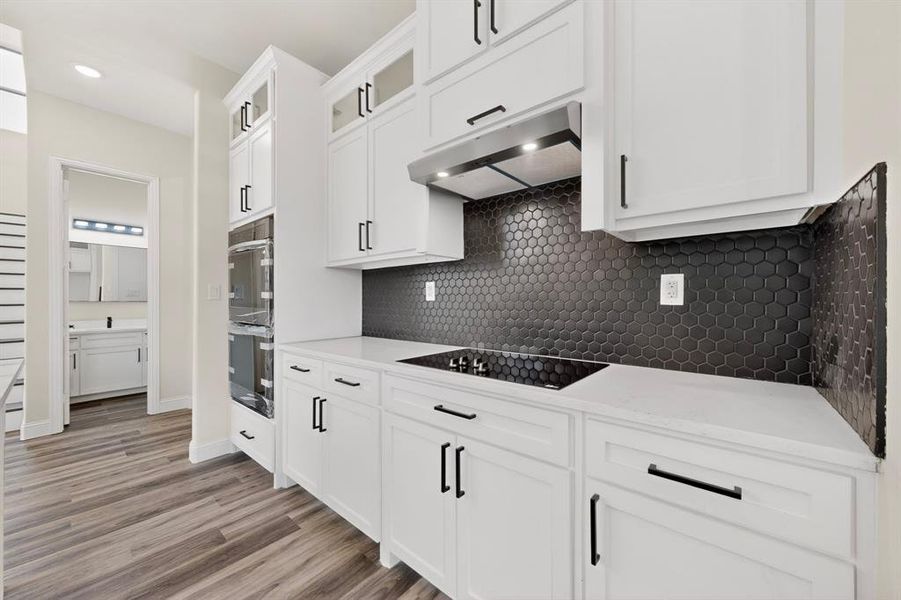 Kitchen featuring white cabinetry with black hardware, white countertops, and a black hexagonal tile backsplash