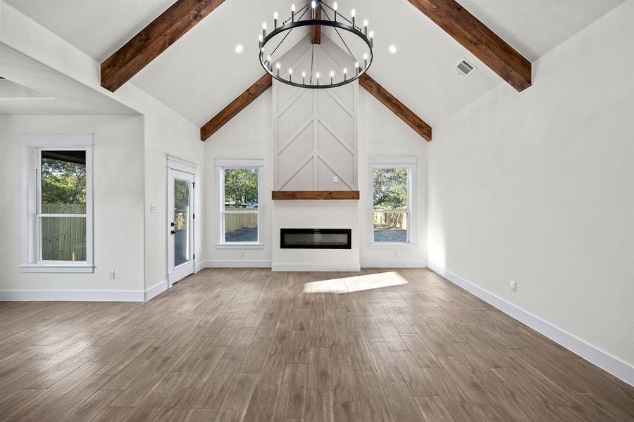 Unfurnished living room featuring high vaulted ceiling, a fireplace, recessed lighting, a chandelier, and wood finished floors