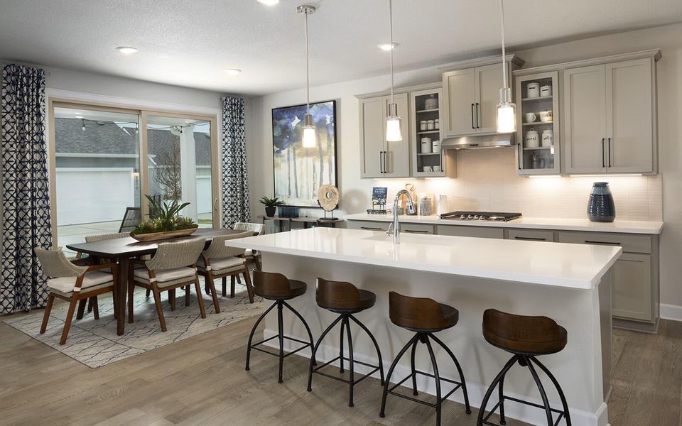 Kitchen with glass insert cabinets, gray cabinets, a kitchen breakfast bar, hanging light fixtures, and light wood finished floors Kitchen with glass insert cabinets, gray cabinets, a kitchen breakfast bar, hanging light fixtures, and light wood finished floors