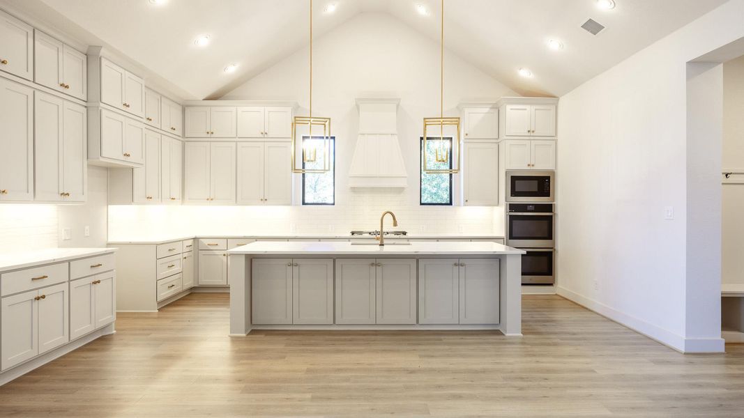 Kitchen with decorative backsplash, an island with sink, decorative light fixtures, light wood-type flooring, and high vaulted ceiling Kitchen with decorative backsplash, an island with sink, decorative light fixtures, light wood-type flooring, and high vaulted ceiling