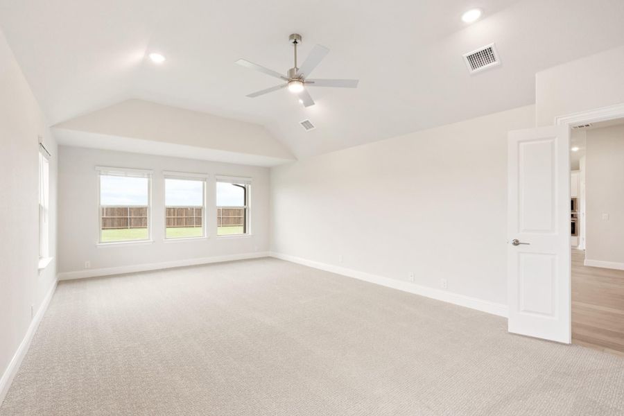 Empty bedroom with vaulted ceiling, ceiling fan, carpet flooring, and triple windows overlooking backyard