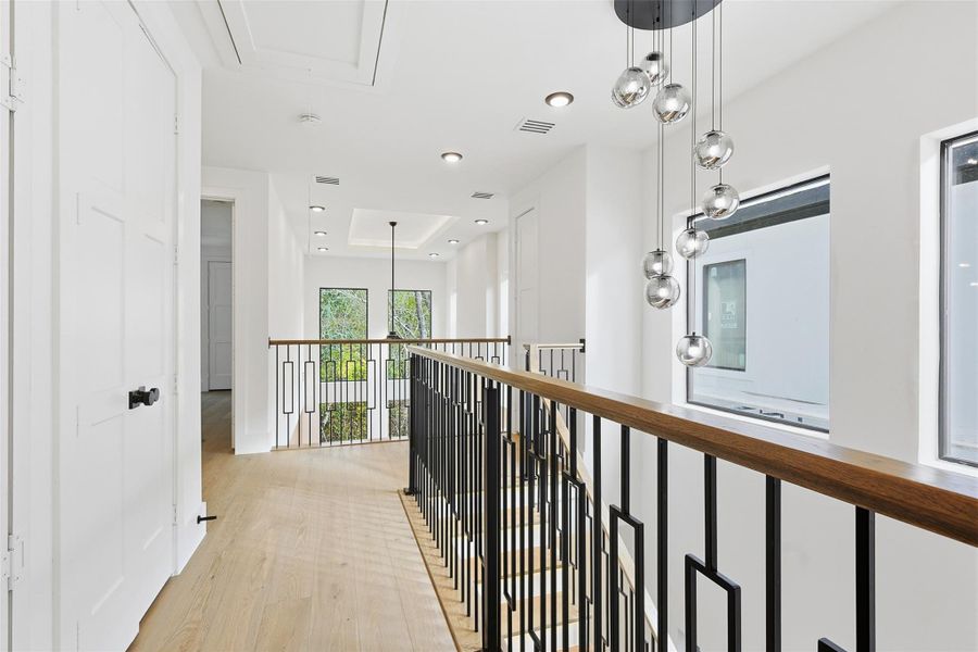 The second-floor landing showcases a minimalist metal railing and a multi-pendant glass light fixture overlooking the entryway.