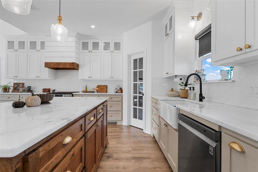 Kitchen with dishwasher, light wood-style floors, light stone counters, glass insert cabinets, and tasteful backsplash