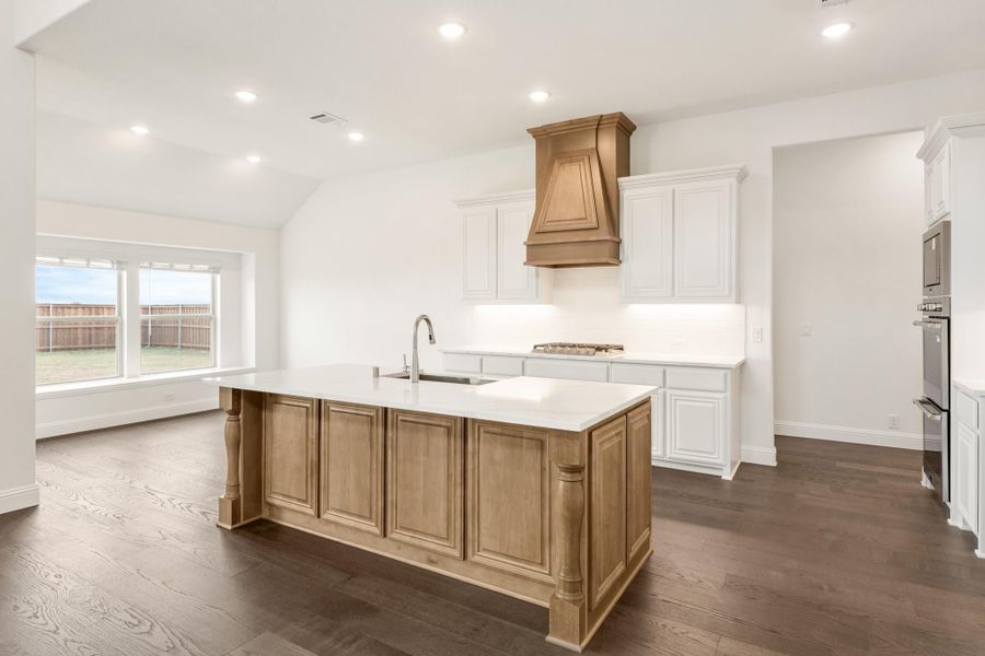 Kitchen with large wood island, white cabinets, wood range hood, and dark hardwood floors