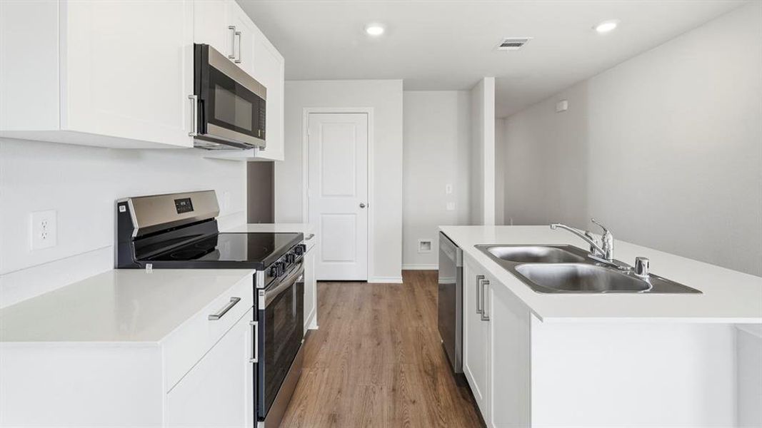 Kitchen with stainless steel appliances, a center island with sink, light countertops, dark wood-type flooring, and white cabinetry
