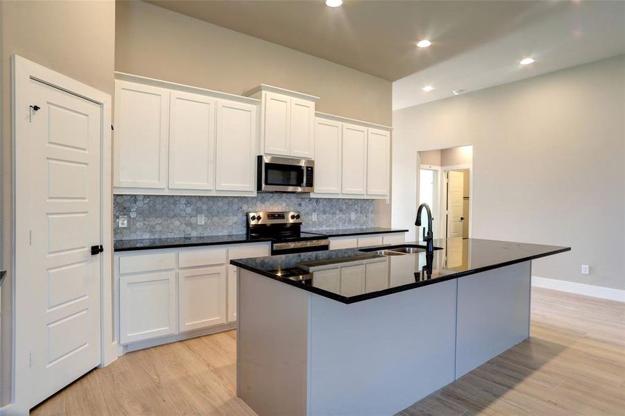 Kitchen with backsplash, white cabinets, a kitchen island with sink, stainless steel appliances, and dark stone counters Kitchen with backsplash, white cabinets, a kitchen island with sink, stainless steel appliances, and dark stone counters