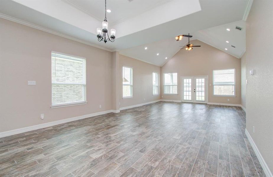 This is a spacious, brightly lit room with high vaulted ceilings, featuring a modern ceiling fan and multiple windows for natural light. The room has a neutral color palette with fresh paint and is finished with stylish tile flooring that resembles wood planks. Glass-paneled doors lead to an outdoor space, enhancing the open feel of the room.