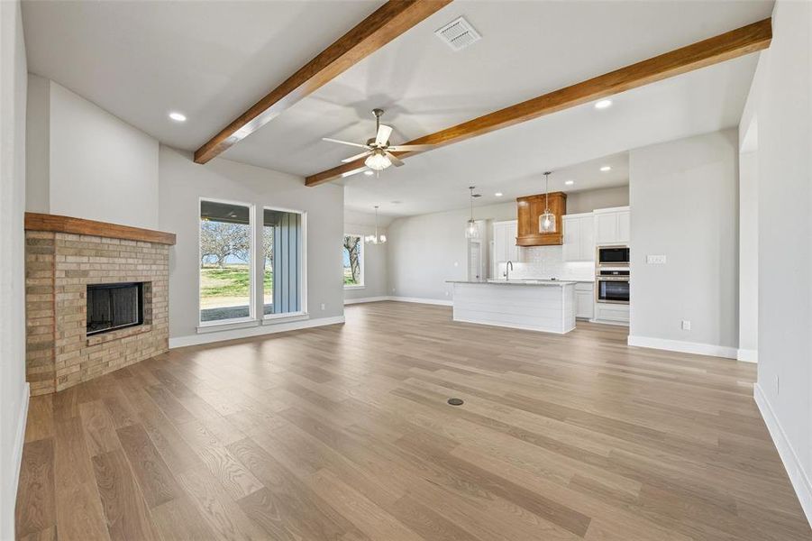 Unfurnished living room featuring ceiling fan, a fireplace, light wood finished floors, beam ceiling, and recessed lighting