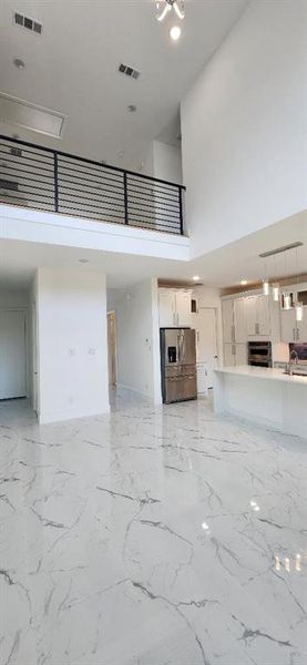 Unfurnished living room featuring a high ceiling, light marble finish floors, and recessed lighting Unfurnished living room featuring a high ceiling, light marble finish floors, and recessed lighting