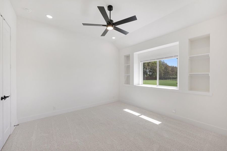 Empty bedroom with vaulted ceiling, black ceiling fan, built-in shelves, and carpet flooring