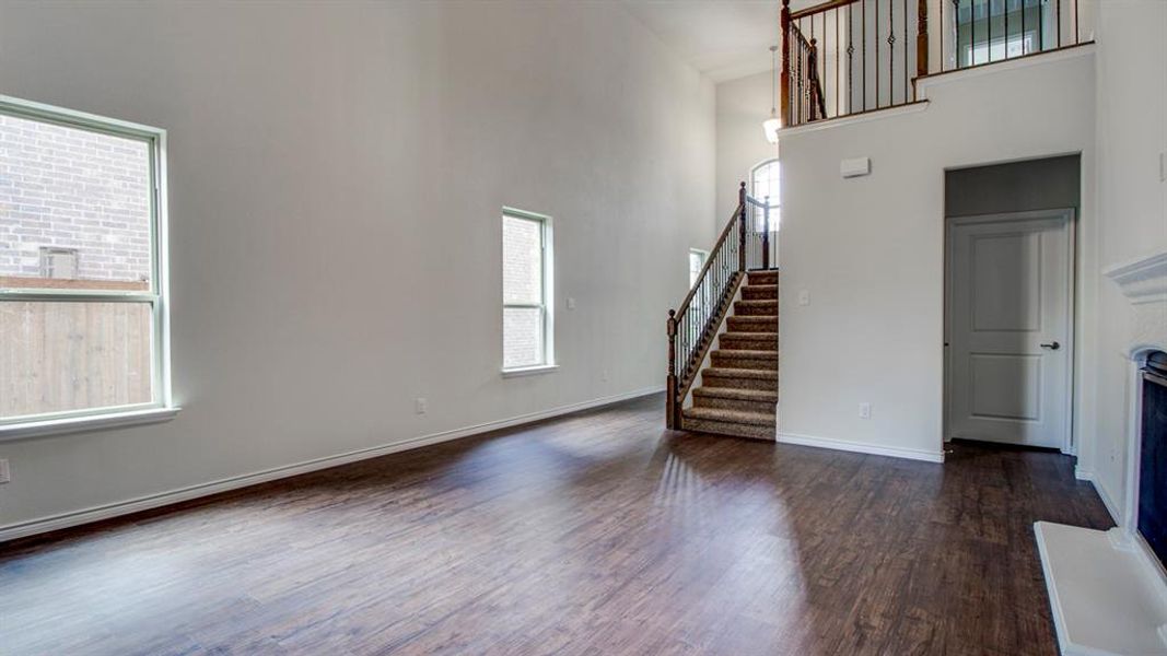 Unfurnished living room with a towering ceiling, dark wood finished floors, stairs, and a fireplace Unfurnished living room with a towering ceiling, dark wood finished floors, stairs, and a fireplace