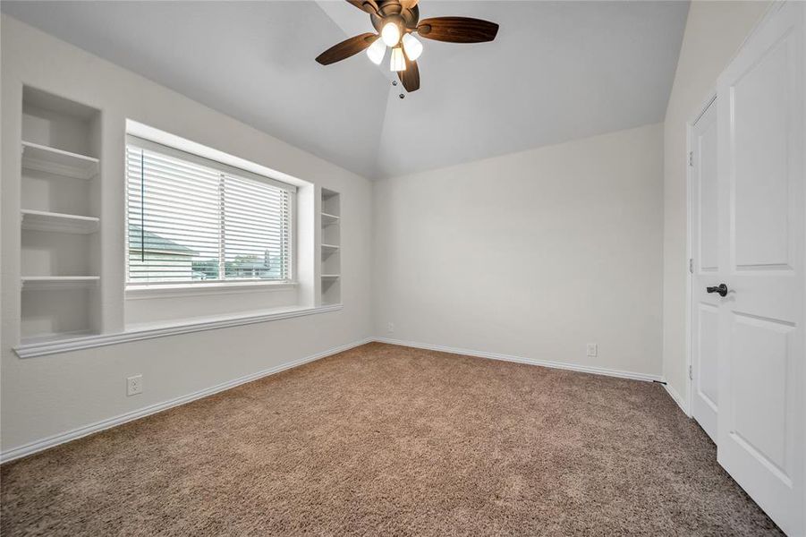 Empty room with built in features, carpet flooring, lofted ceiling, and ceiling fan Empty room with built in features, carpet flooring, lofted ceiling, and ceiling fan