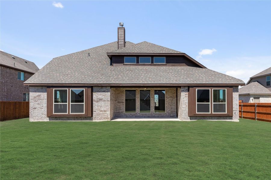 Rear exterior of brick home with covered patio, large windows, and fenced backyard lawn Rear exterior of brick home with covered patio, large windows, and fenced backyard lawn