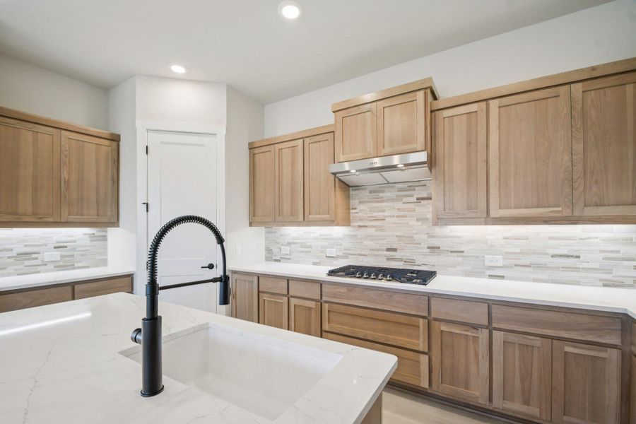 Kitchen with decorative backsplash, light stone counters, under cabinet range hood, recessed lighting, and stainless steel gas stovetop