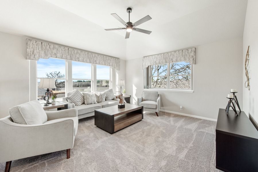Living room with gray sofa, ceiling fan, carpet flooring, and large windows with outdoor views
