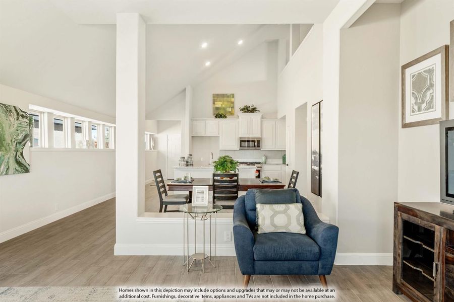 Open-concept living area with vaulted ceilings, hardwood floors, and kitchen visible in background