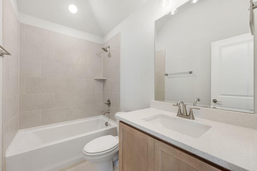 Bathroom with tiled tub-shower combo, wood vanity with quartz countertop, and large mirror