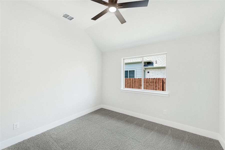 Empty bedroom with vaulted ceiling, ceiling fan, gray carpet, and single window